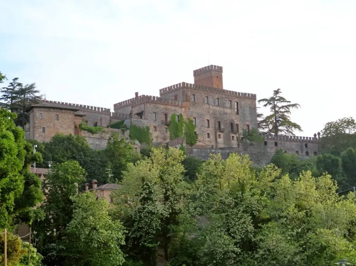 Castello medievale su una collina, circondato da alberi verdi. Un esempio dei suggestivi borghi vicino Parma.