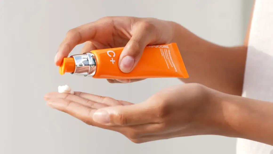 Mani che dosano una crema con vitamina C sulla pelle, per un trattamento illuminante e antiossidante.