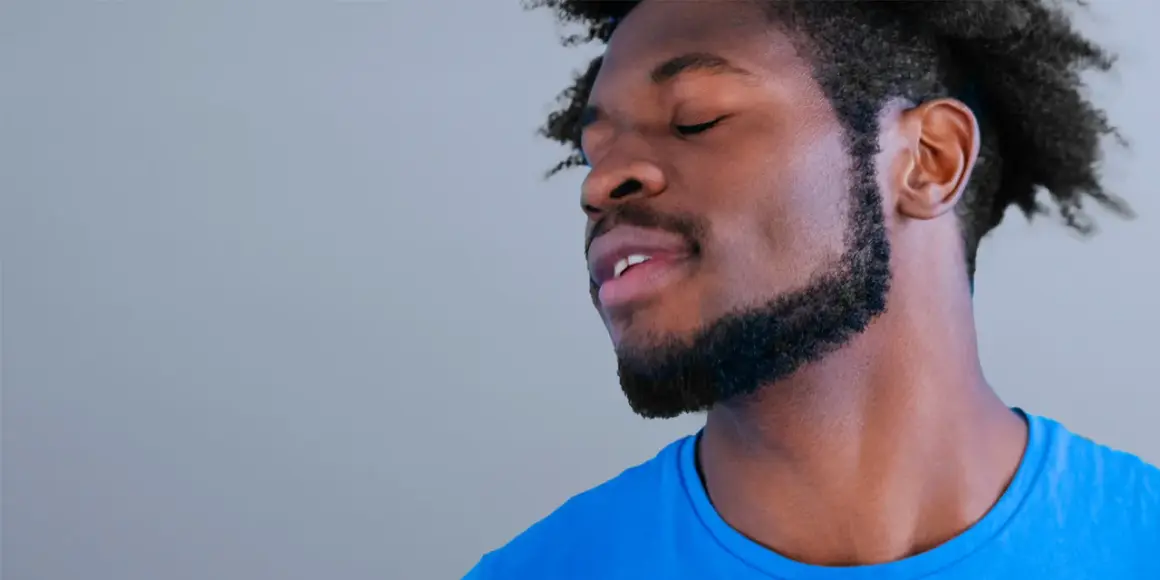Un homme avec une barbe collier épaisse, les yeux fermés, porte un t-shirt bleu vif.