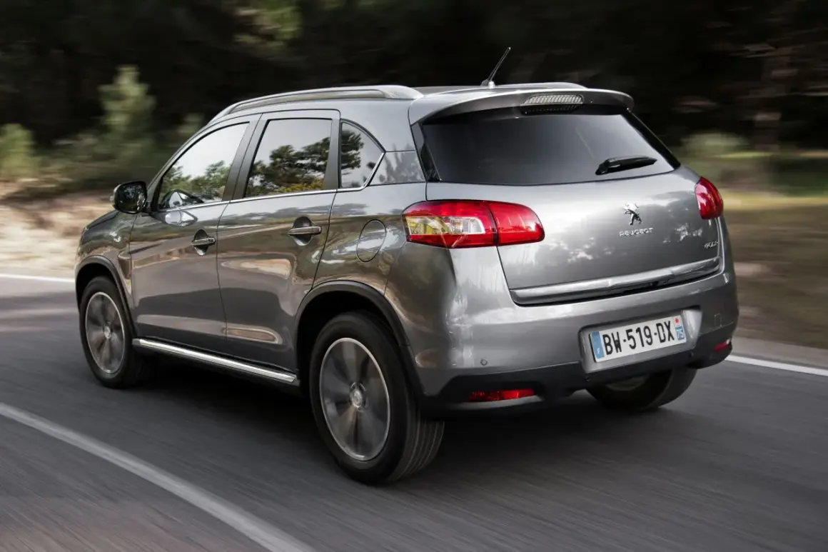 Srebrny Peugeot 4008 jedzie po drodze wśród drzew.