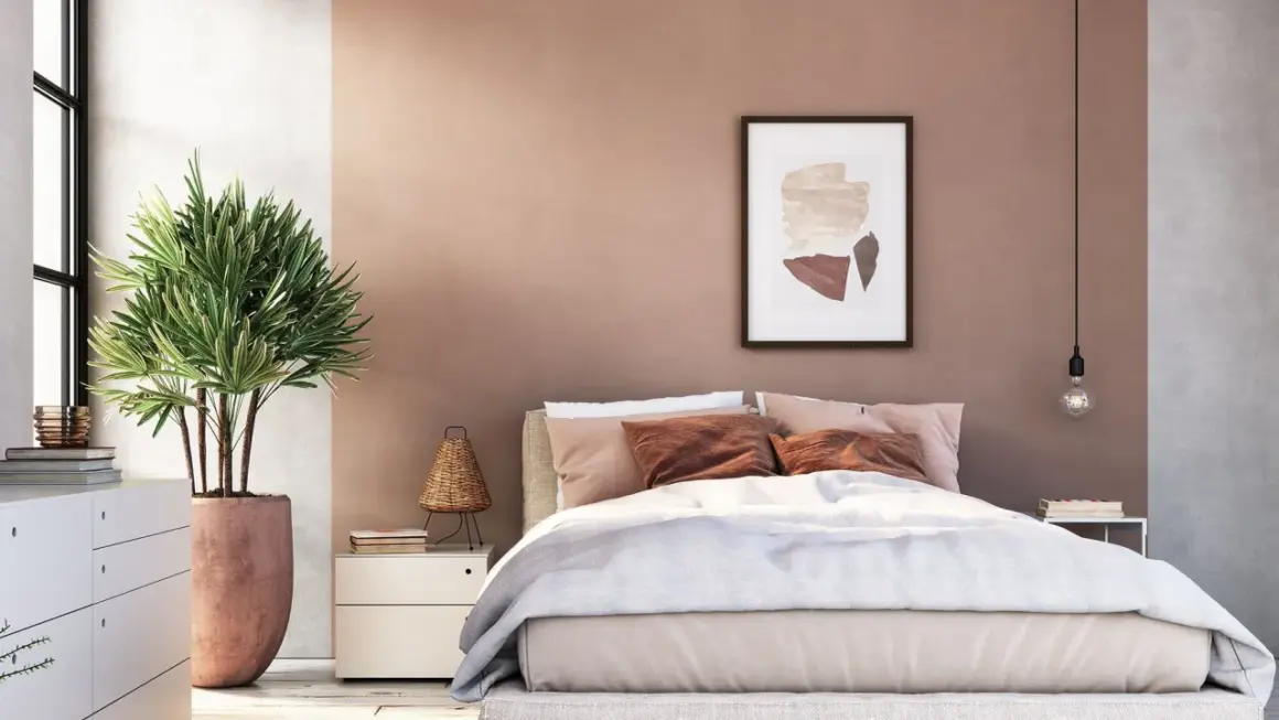 Gemütliches Schlafzimmer mit sanfter, rosafarbener Wandfarbe. Ein großes Bett mit beiger Bettwäsche und braunen Kissen lädt zum Entspannen ein.