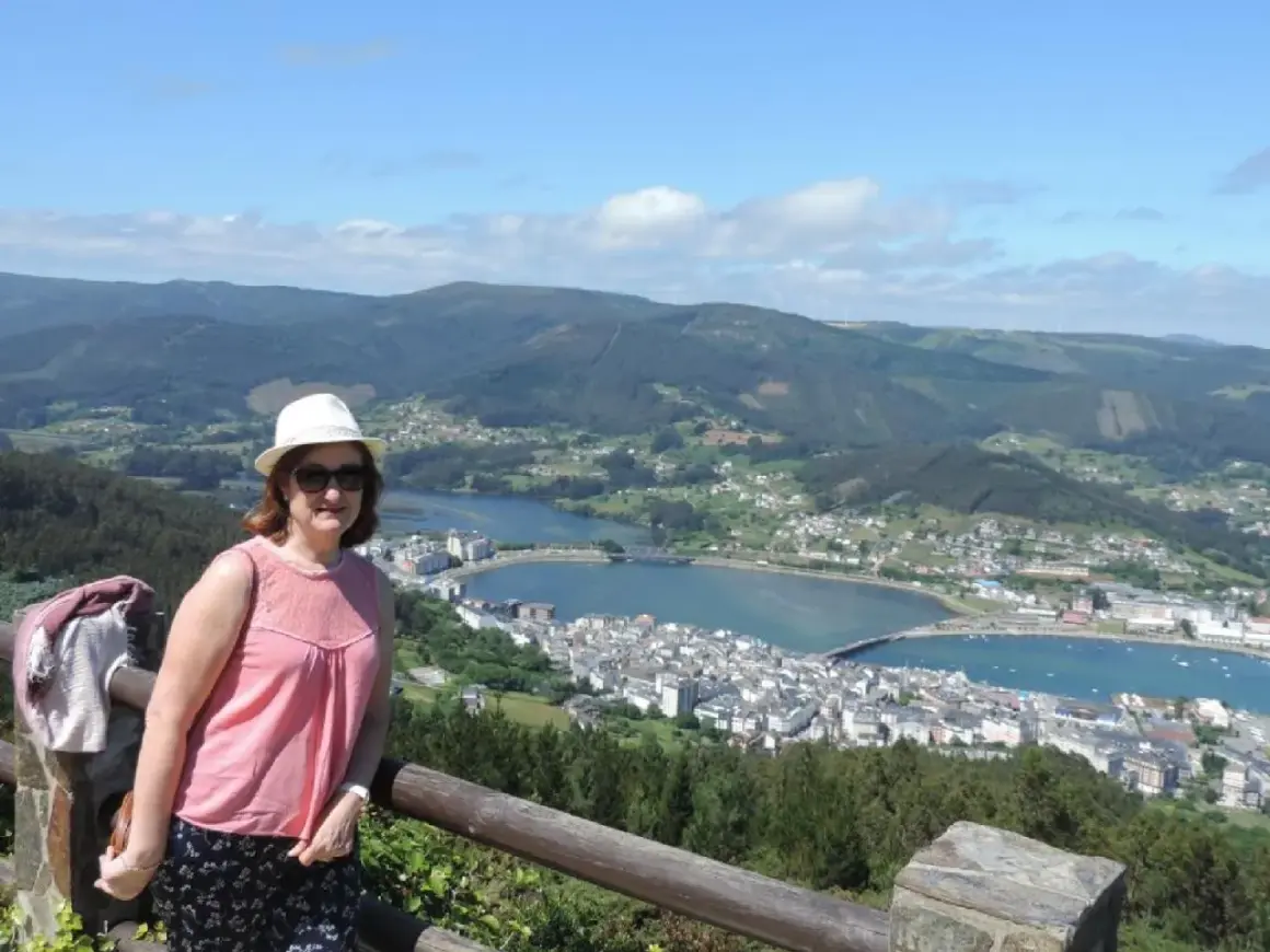 Mujer con sombrero blanco y blusa rosa posa en el mirador de San Roque, disfrutando de la vista panorámica de la ría y el pueblo.