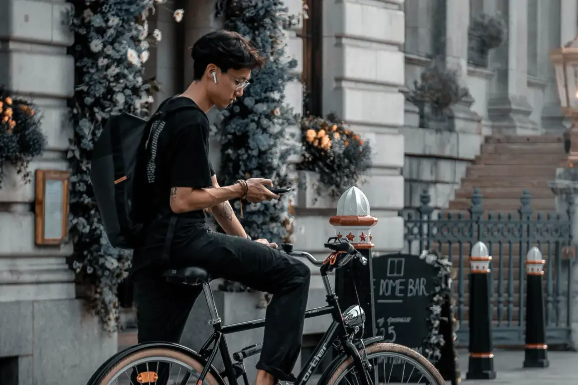 Jonge man op fiets met rugzak, kijkend op zijn telefoon. Is een fietser altijd beschermd in het verkeer?