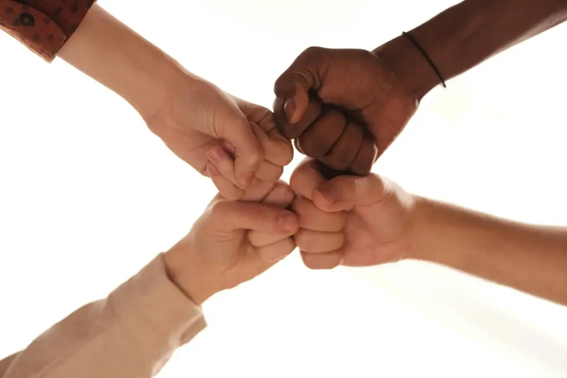 Vier Fäuste stoßen zusammen, ein Symbol für **diversity in der pflege**. Hände verschiedener Hautfarben vereinen sich in einem Zeichen der Solidarität und des Zusammenhalts.