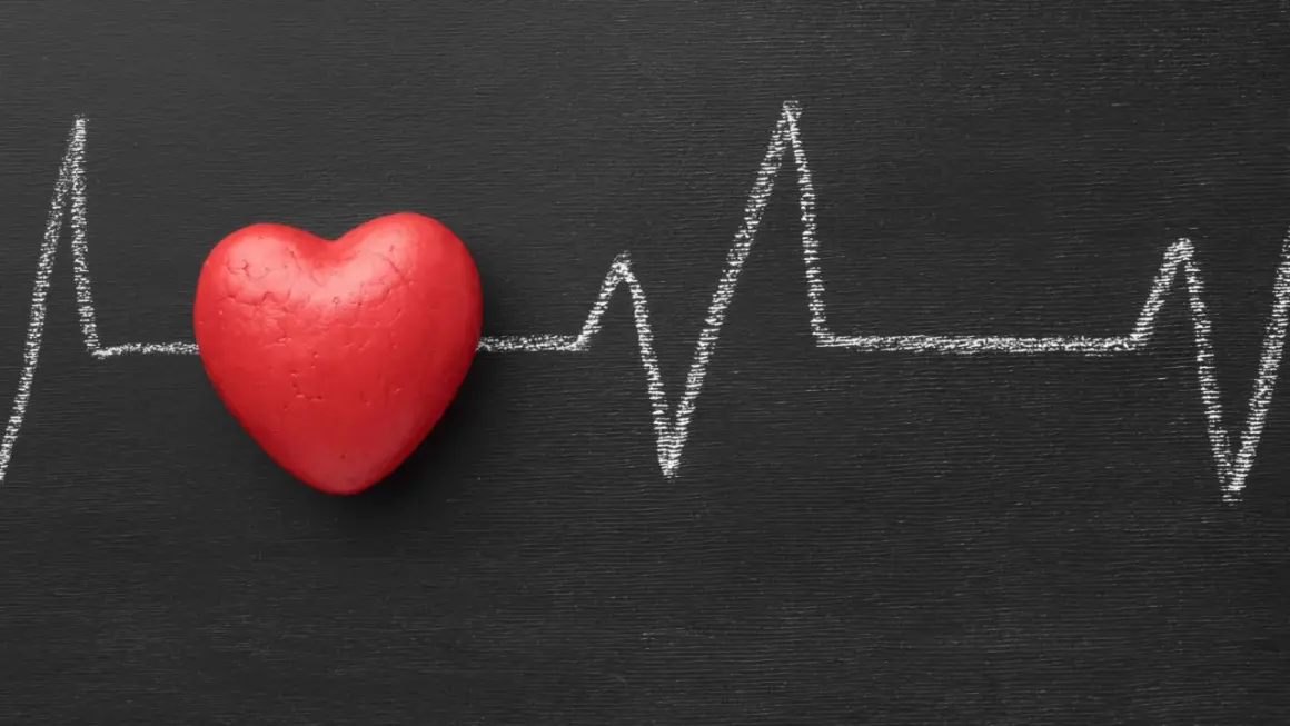 Cuore rosso su lavagna nera con tracciato ECG. Un simbolo di cosa fa alzare la pressione.