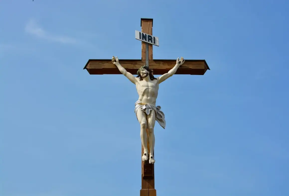 Figurka Jezusa na drewnianym krzyżu pod błękitnym niebem.