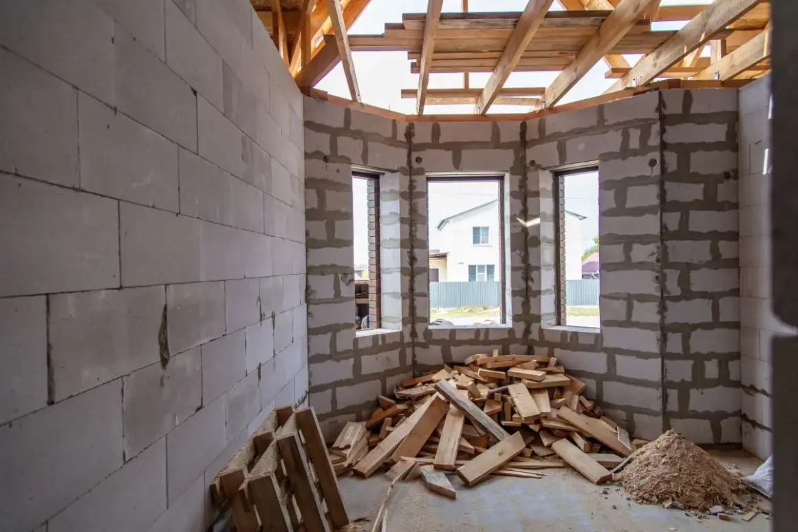 Interno di una casa in costruzione con muri in blocchi di cemento, tetto in legno e cumuli di legname. Forse un caso di abuso edilizio prescrizione.