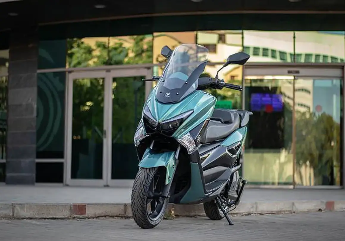 Scooter onex motos color verde menta, con parabrisas alto, estacionada frente a un edificio moderno con puertas de cristal.