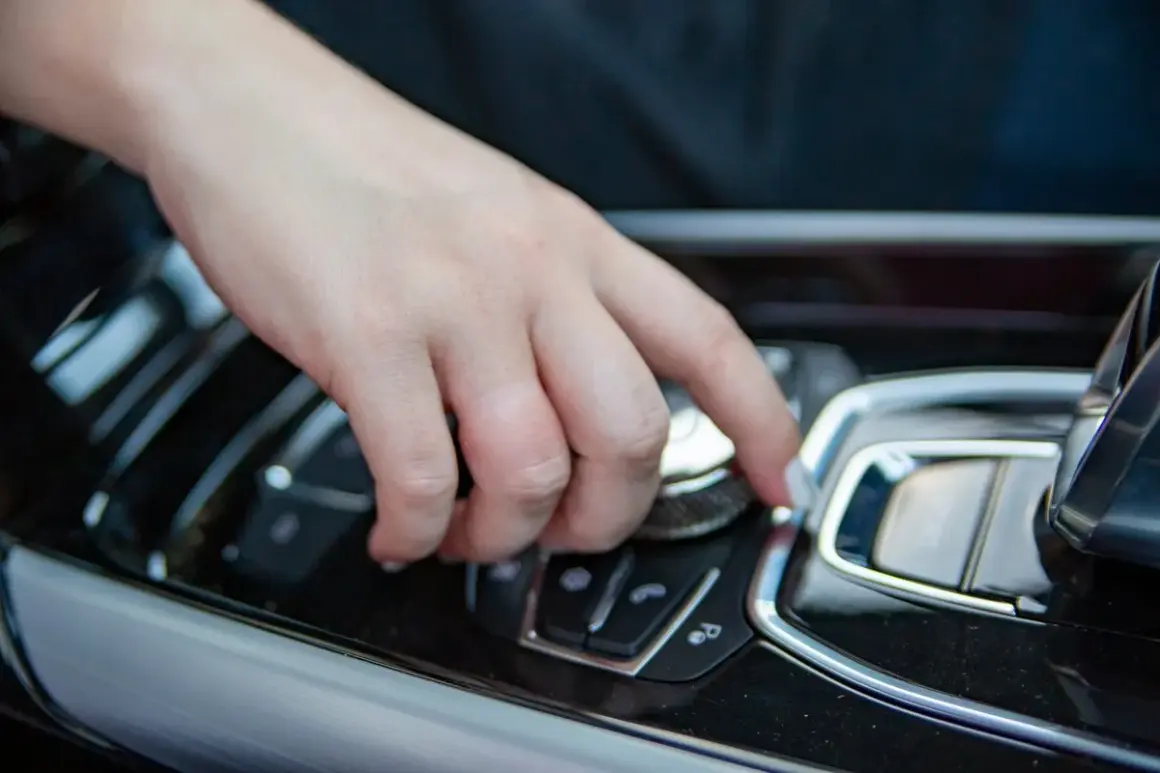 Main d'une personne actionnant un bouton sur la console centrale d'une voiture, peut-être pour savoir comment débloquer un frein à main automatique.
