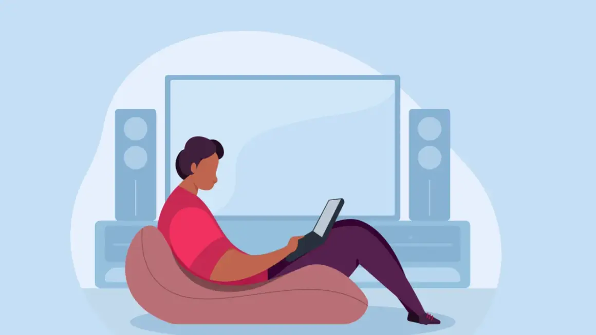 Person im Sessel mit Laptop, vor einem großen Bildschirm und Lautsprechern. Ein Beispiel für hybrides Arbeiten, flexibel und bequem.