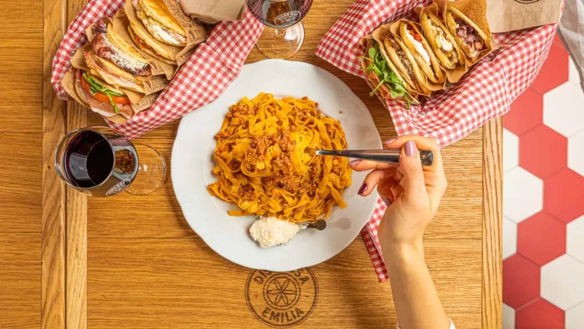 Tagliatelle al ragù, un classico italiano. Accanto, piadine farcite e un bicchiere di vino rosso.