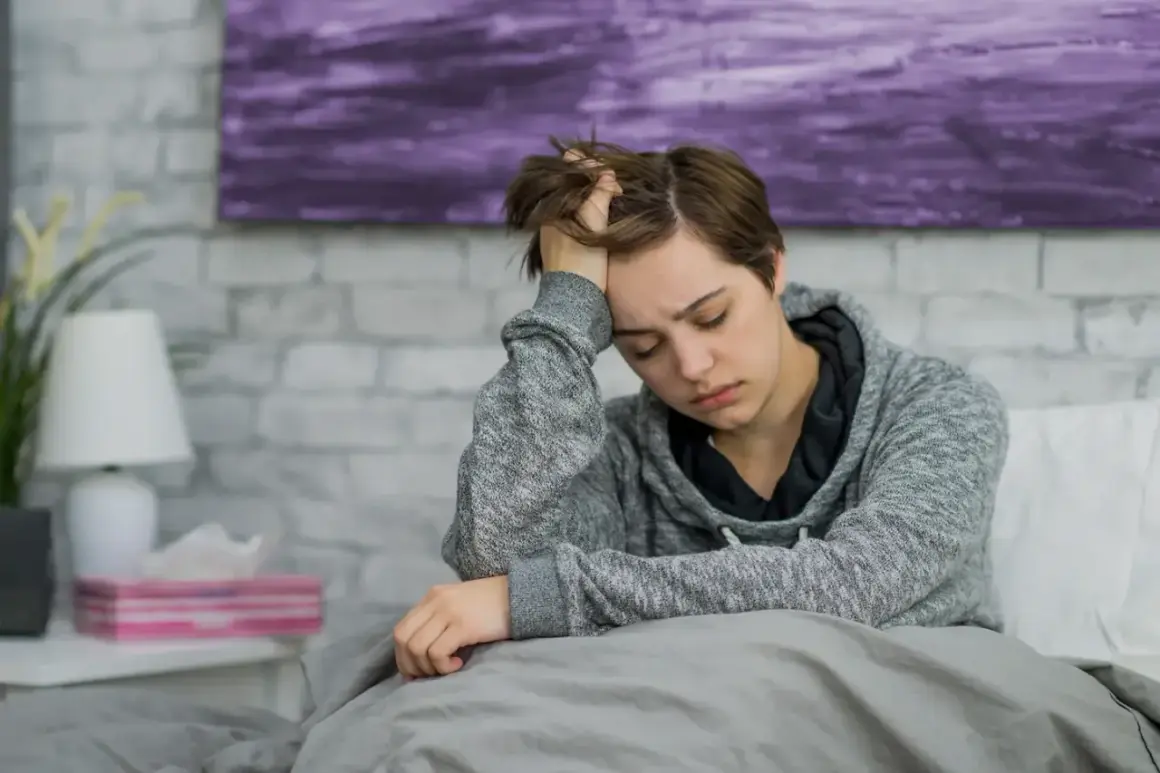 Müde Person im Bett, die sich an den Kopf fasst. Mögliche Anzeichen von Blutkrebs wie Müdigkeit und Kopfschmerzen sollten ernst genommen werden.