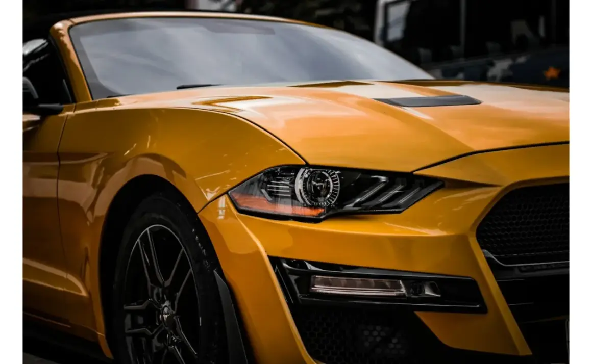 Żółty Ford Mustang z błyszczącym lakierem, jakby był pomalowany farbą akrylową, z detalami reflektorów i grillem.
