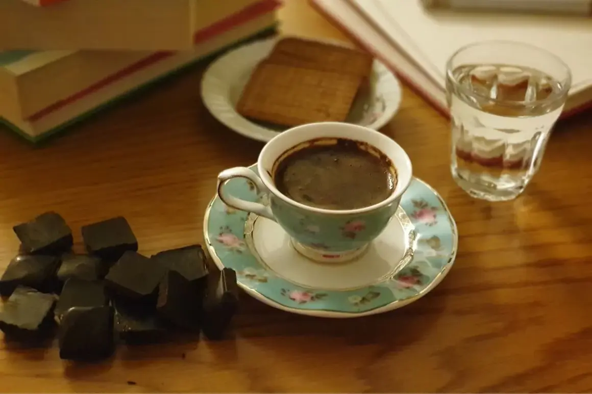 En kopp mörkt, aromatiskt kaffe med garvsyra, bredvid mörk choklad och en bok. En perfekt stund för avkoppling.
