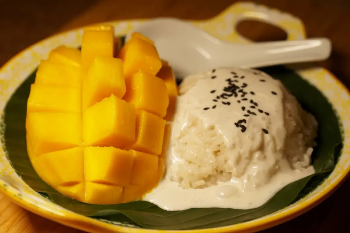Ein Teller mit süßem Mango Sticky Rice, garniert mit Kokosmilch und Sesam. Ein köstlicher Nachtisch!