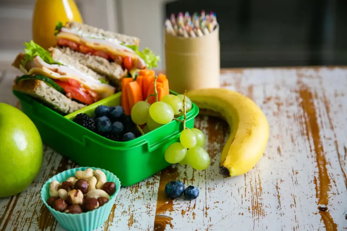 Gesunde Lunchbox mit Sandwiches, Beeren, Trauben, Karotten, Nüssen und Obst. Perfekt für kalorienarme Snacks unterwegs.