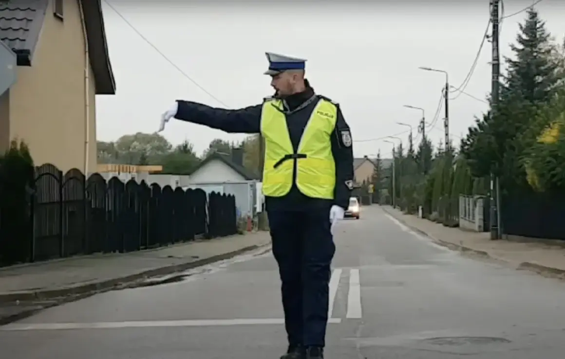 Policjant w kamizelce odblaskowej kieruje ruchem na ulicy, wskazując ręką kierunek.