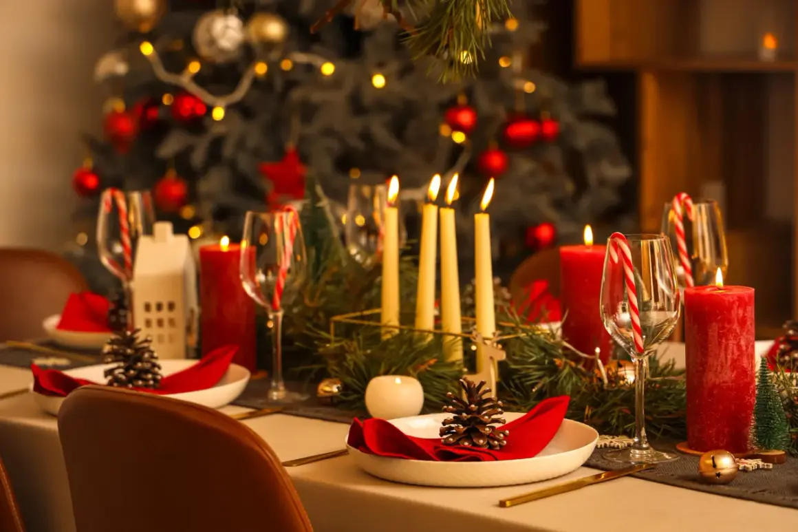 Uroczysta wigilia w restauracji: pięknie nakryty stół z czerwonymi świecami, szyszkami i choinką w tle.