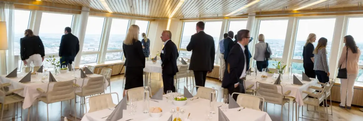 Människor i affärs kläder njuter av utsikten från en restaurang. En turning torso visning av staden.