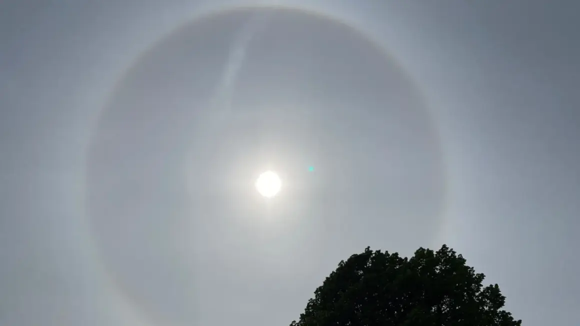 En vacker solring runt solen, ett optiskt fenomen som skapar en cirkel av ljus. En grönaktig prick syns också nära solen.