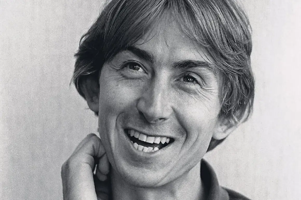 Black and white close-up portrait of Mark Hollis of Talk Talk smiling with his hand near his face.