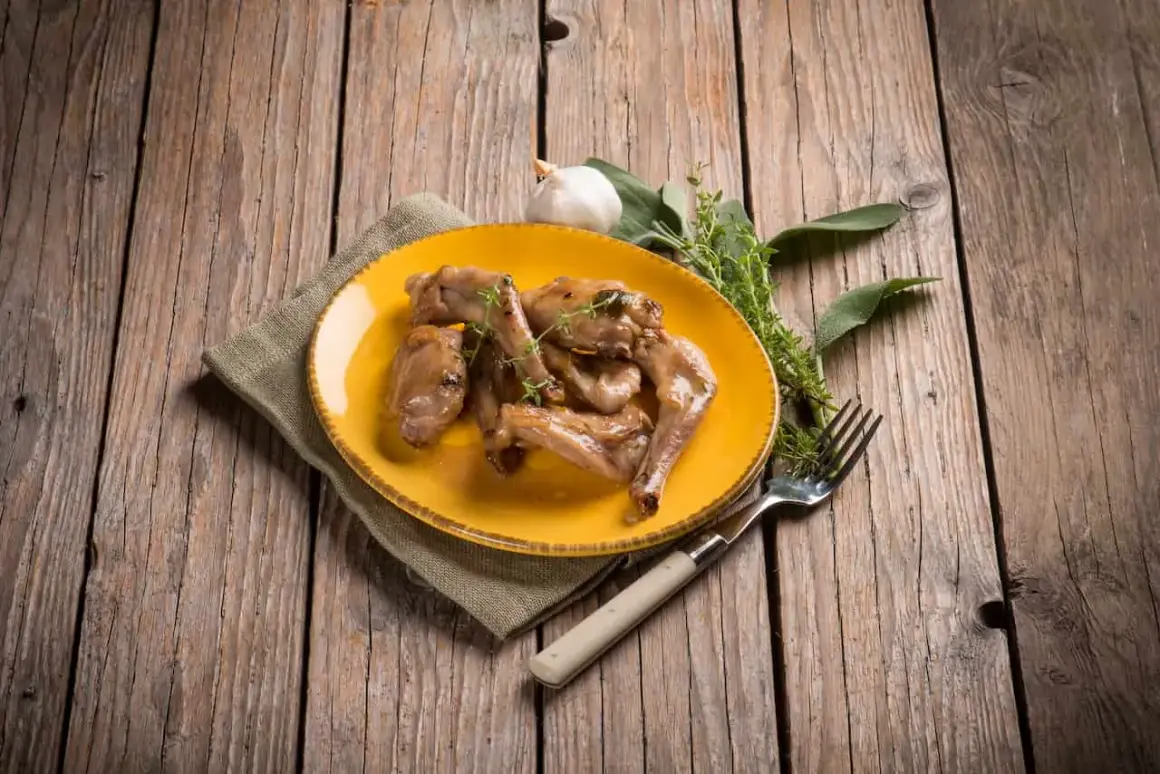 Sabroso conejo al ajillo servido en plato amarillo, acompañado de hierbas frescas y un tenedor, sobre una mesa de madera rústica.