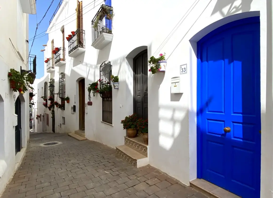 Calle empedrada con casas blancas y puertas azules vibrantes. Un lugar perfecto para descubrir qué hacer en Mojácar.