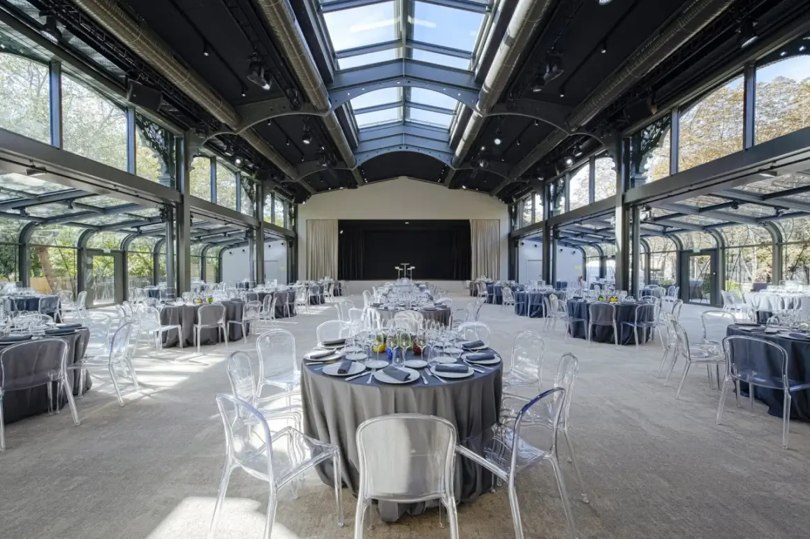 Salle de réception lumineuse au pavillon Gabriel, tables rondes dressées sous une verrière, chaises transparentes.