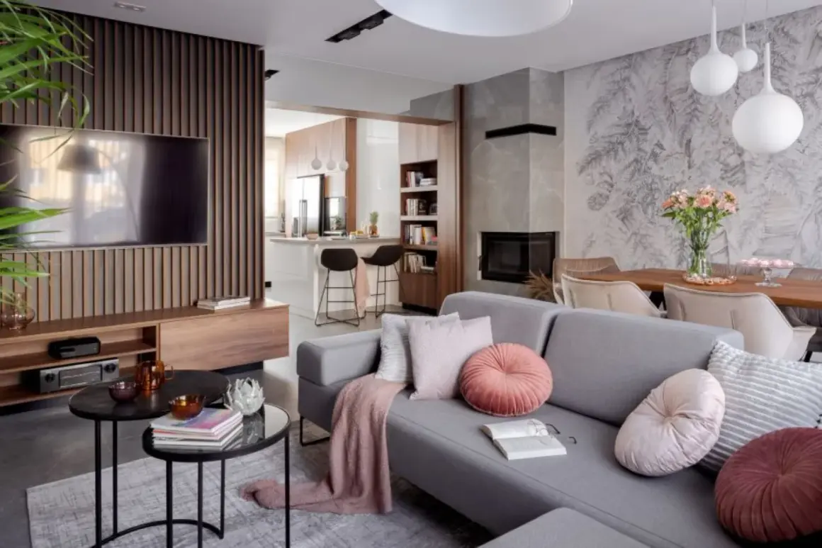 Nowoczesny salon z szarą sofą, kominkiem i otwartą kuchnią. Galeria wnętrz zachwyca detalami.