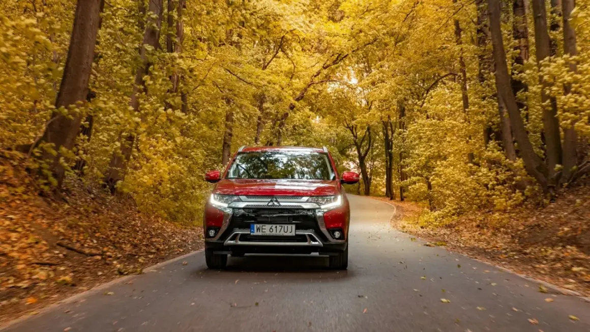 Czerwony Mitsubishi Outlander na jesiennej drodze wśród złotych liści. Sprawdź jego spalanie w podróży!
