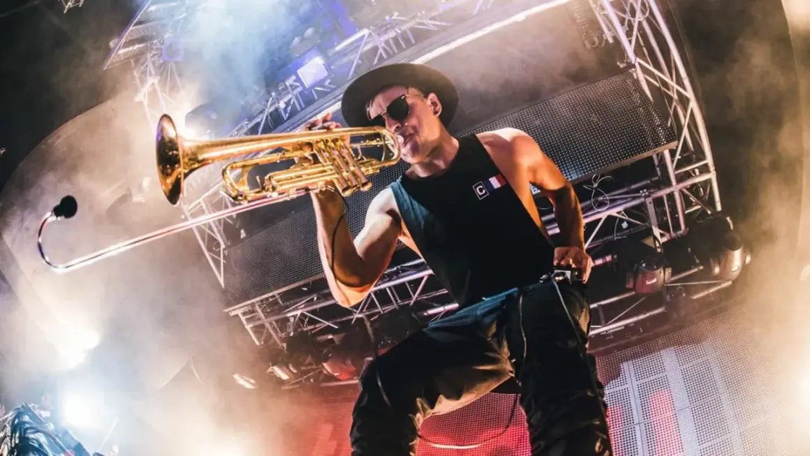 Timmy Trumpet gra na trąbce na scenie w Polsce, otoczony dymem i światłami.