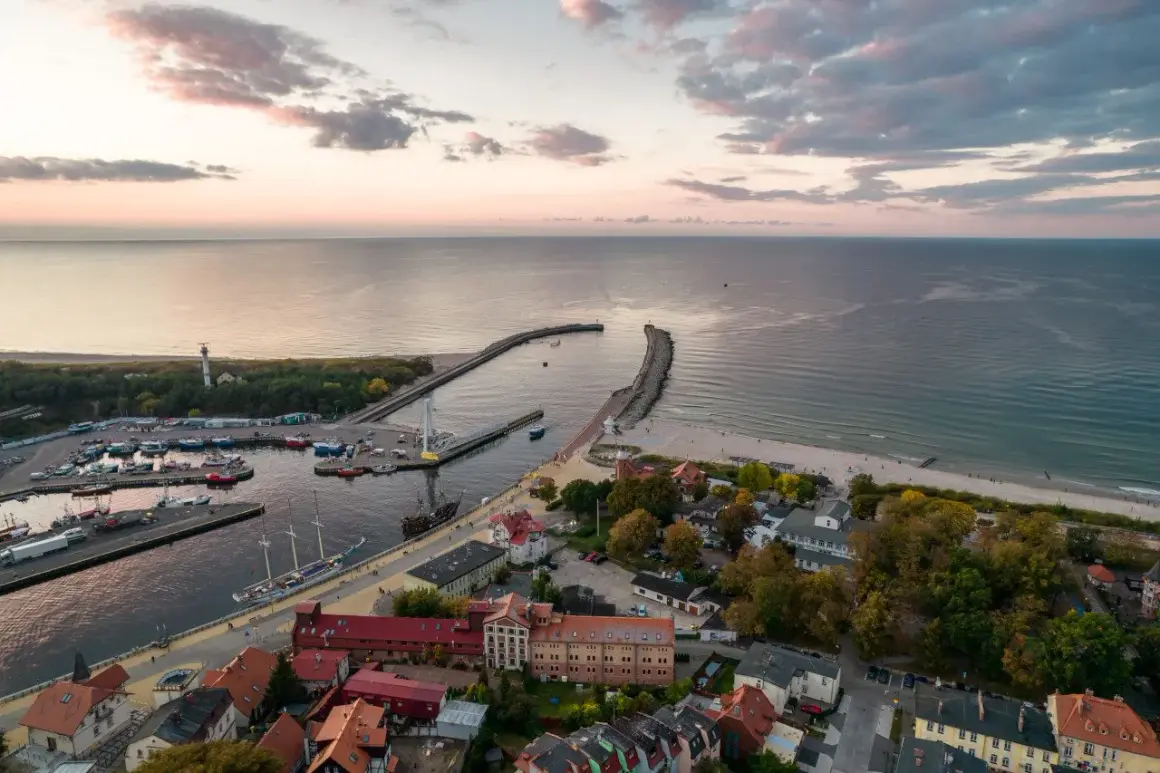 Widok z lotu ptaka na port i plażę w Ustce. Widać liczne łodzie, latarnię morską i falochrony. To idealne miejsce na odkrywanie ustka atrakcje.