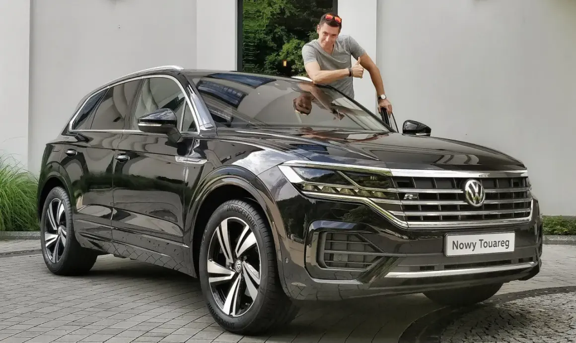 Mężczyzna z kciukiem w górę przy nowym, czarnym Volkswagenie Touareg. Jego imponujące wymiary robią wrażenie.