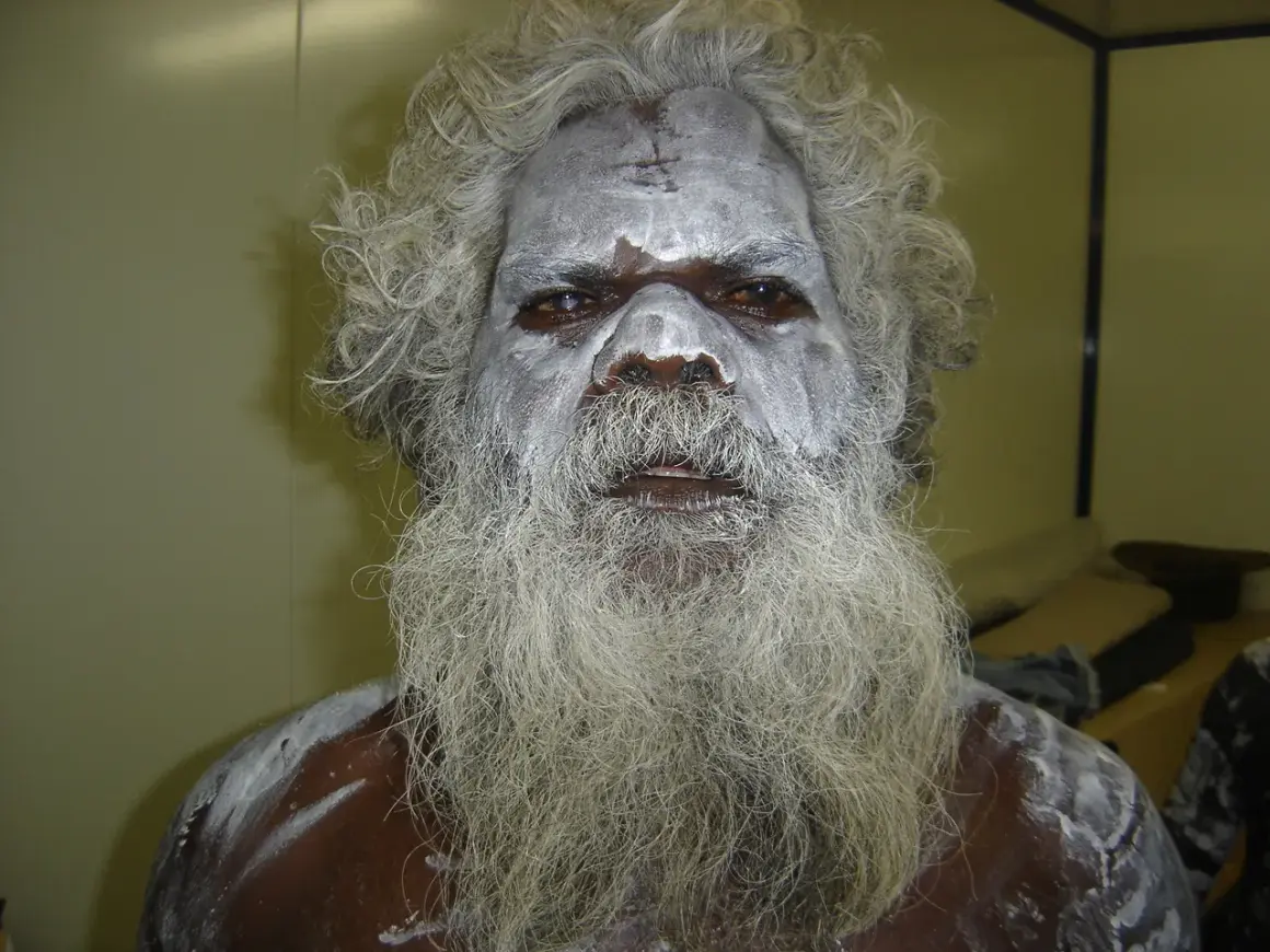 En aboriginal model med vitt ansiktsmåleri och långt grått skägg.