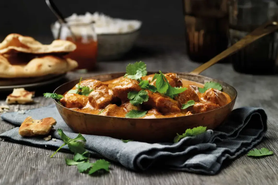 En skål med krämig tikka masala, toppad med färsk koriander, serveras med naanbröd och ris.