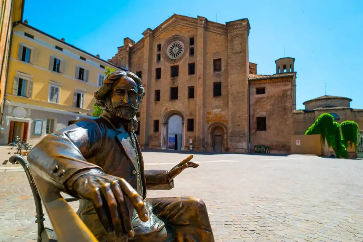 Statua in bronzo di un uomo barbuto, un monumento in Emilia Romagna, con una chiesa in mattoni sullo sfondo.