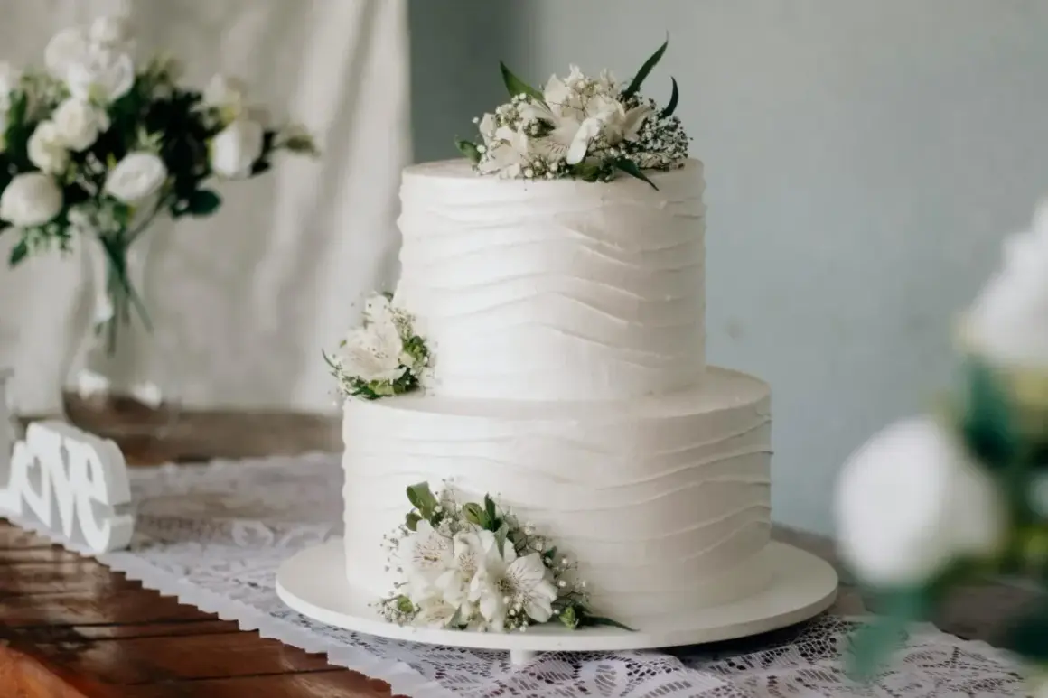 Elegancki tort komunijny, idealny na 20 osób. Białe kwiaty zdobią dwupoziomowe ciasto.