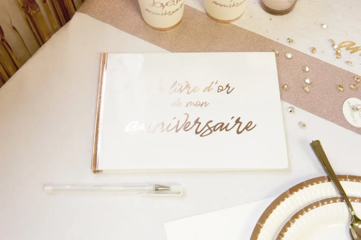 Un livre d'or de mon anniversaire, prêt à recueillir les vœux les plus doux. Un stylo blanc et des décorations dorées complètent la scène festive.