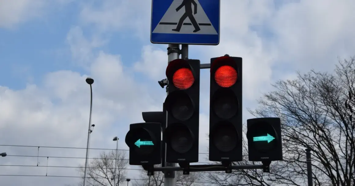 Sygnalizacja świetlna: czerwone światła dla jazdy prosto, zielona strzałka w lewo. Czy na strzałce w lewo można zawracać? Znak przejścia dla pieszych.