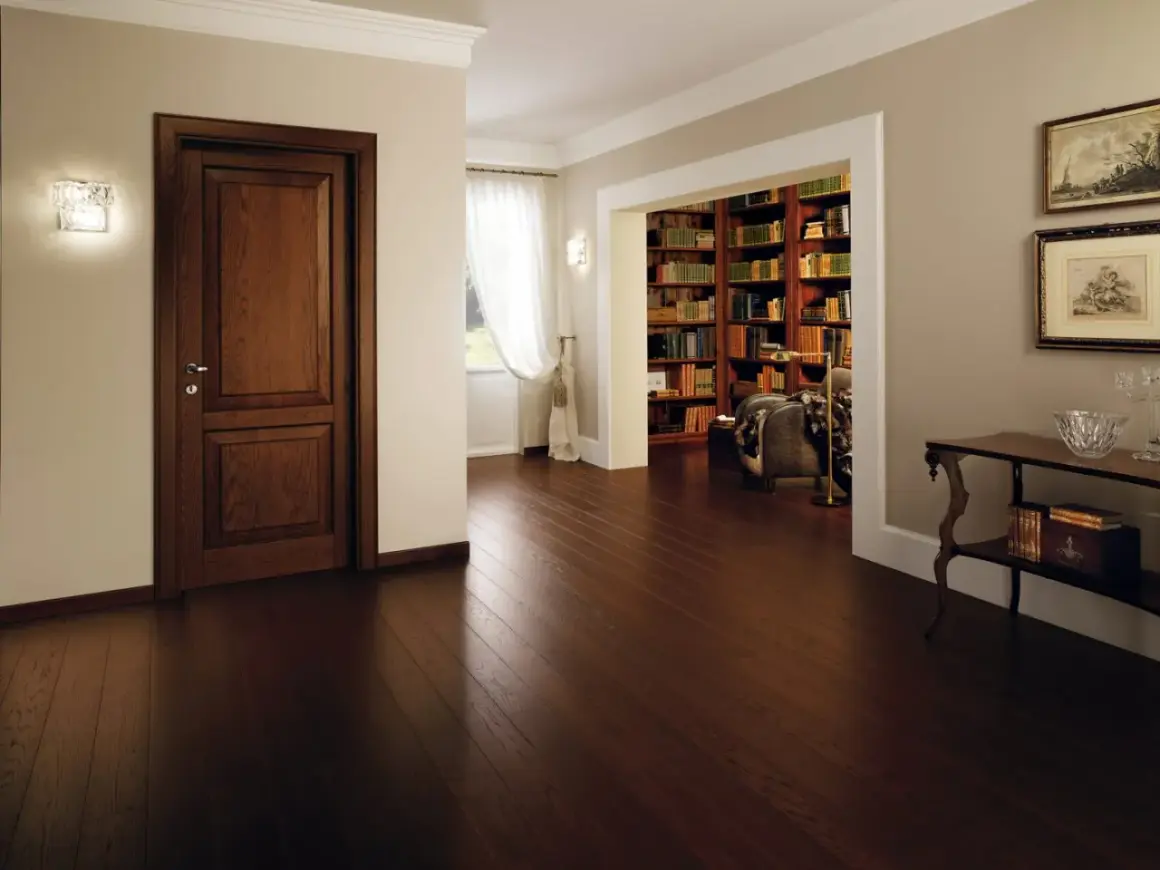Un elegante corridoio con un battiscopa diverso dalle porte in legno scuro, che conduce a una biblioteca ricca di libri.