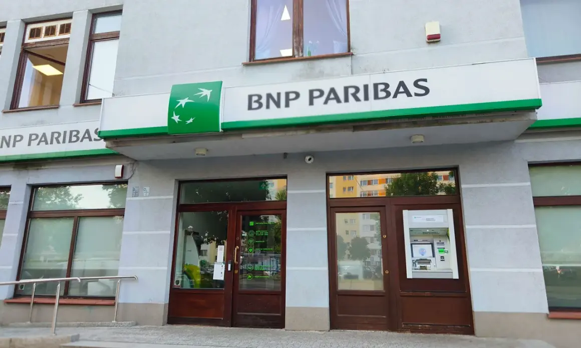 Wejście do placówki banku BNP Paribas z zielonym logo i napisem. Obok drzwi znajduje się bankomat.