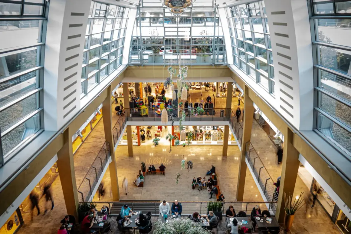 Blick in ein helles Einkaufszentrum in Bergisch Gladbach mit vielen Besuchern, Geschäften und Sitzbereichen.