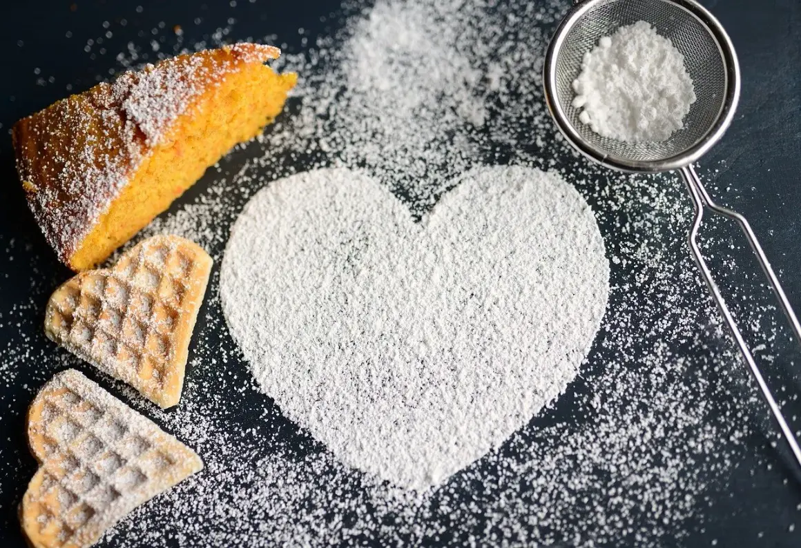 A slice of cake, heart-shaped cookies, and a heart shape made of powdered sugar on a dark surface.