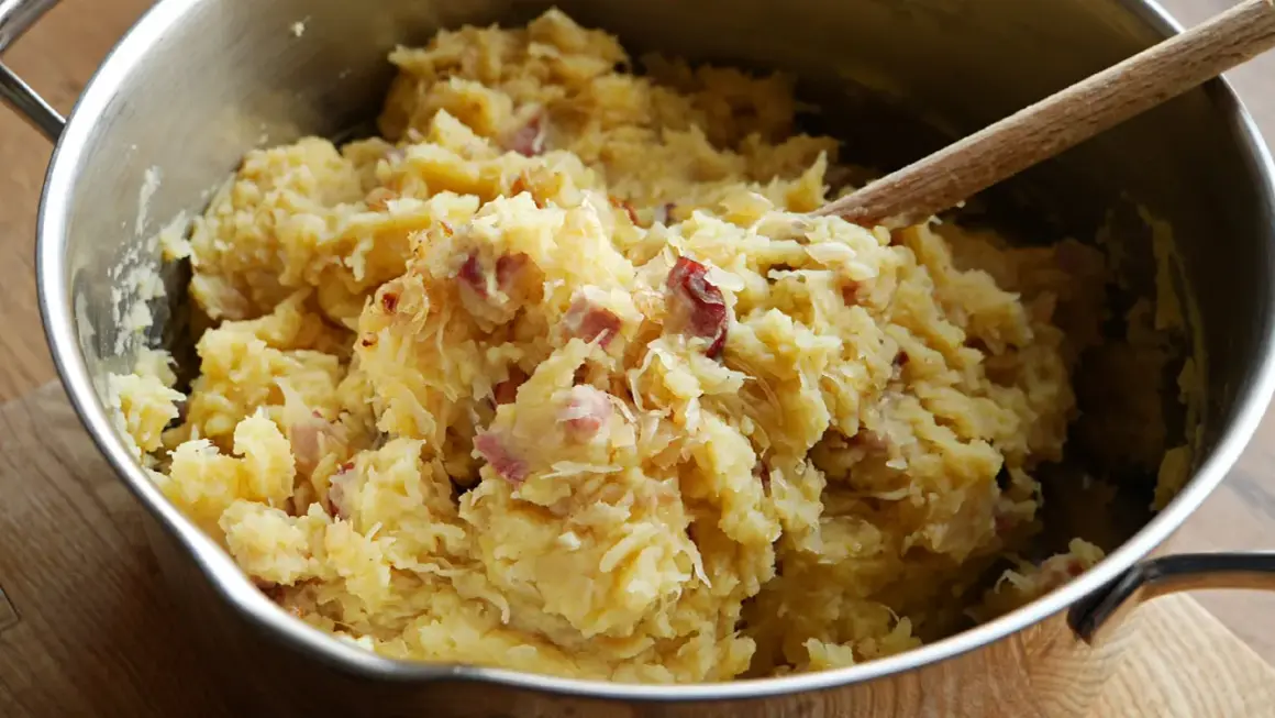 Panczkraut w garnku, gotowy do podania. Drewniana łyżka miesza ziemniaczaną masę z kawałkami boczku.