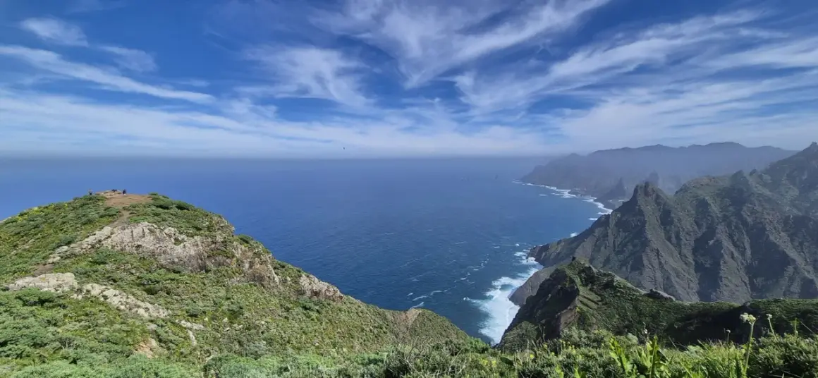 Vista del Roque de Tábarno, un promontorio verde y rocoso que se adentra en el mar azul bajo un cielo nublado.