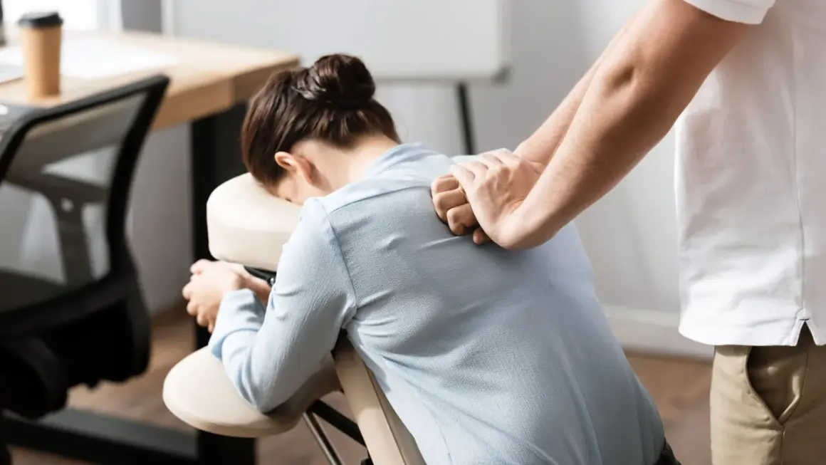 Un masseur offre des massages en entreprise à une femme assise sur une chaise ergonomique, soulageant les tensions du dos.
