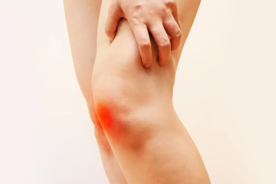 Mano che preme sul ginocchio con un'area rossa che indica dolore al ginocchio a letto.