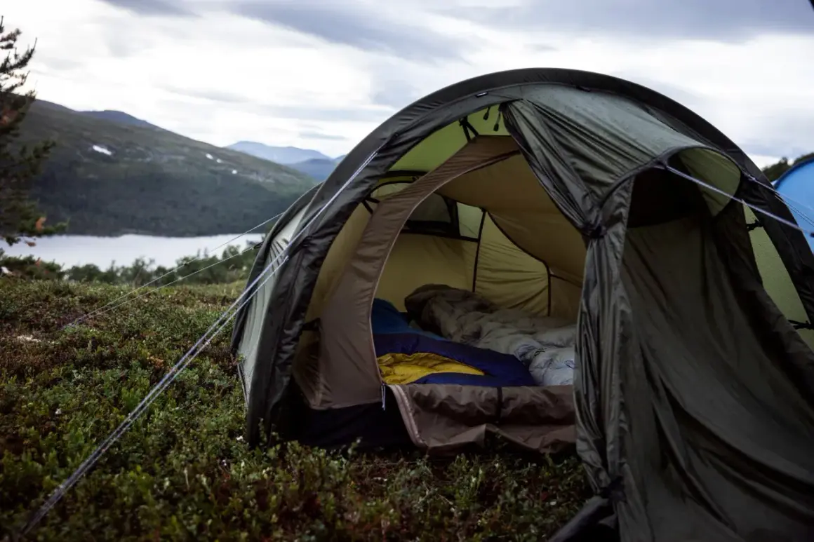 En öppen tält med sovsäckar redo för natten. En mysig känsla av värme i tält utan el, med en sjö och berg i bakgrunden.