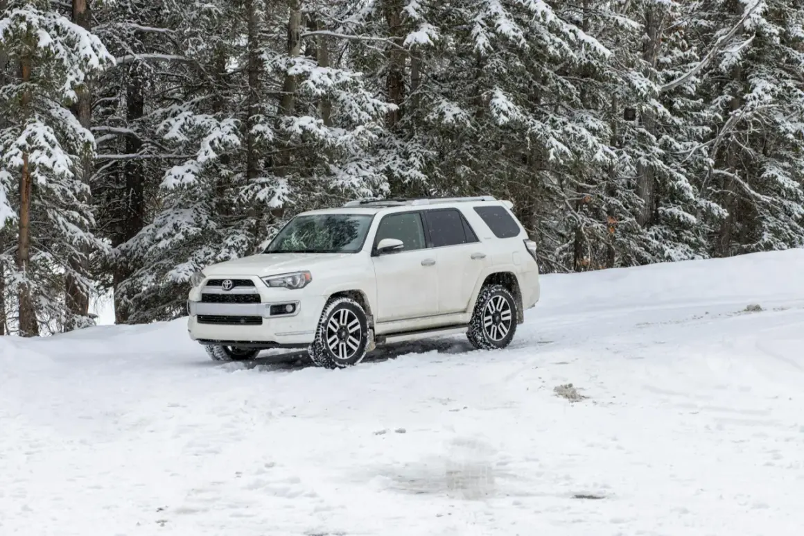 Biały SUV z napędem **awd** stoi na zaśnieżonej drodze w lesie.