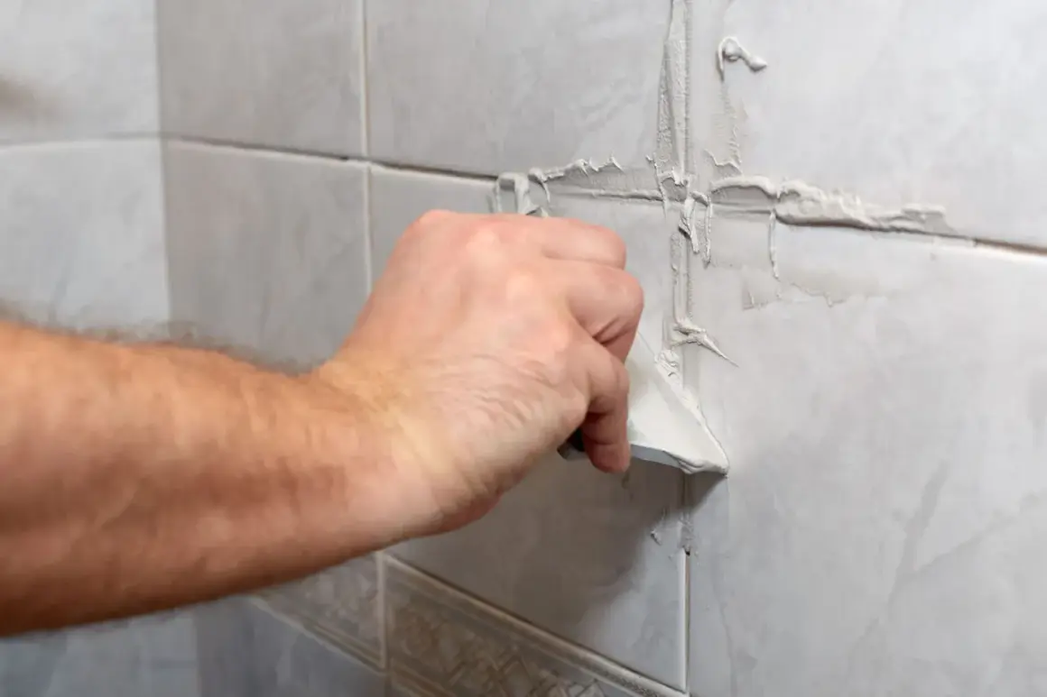 Main tenant utilise une spatule pour refaire le joint du carrelage mural.